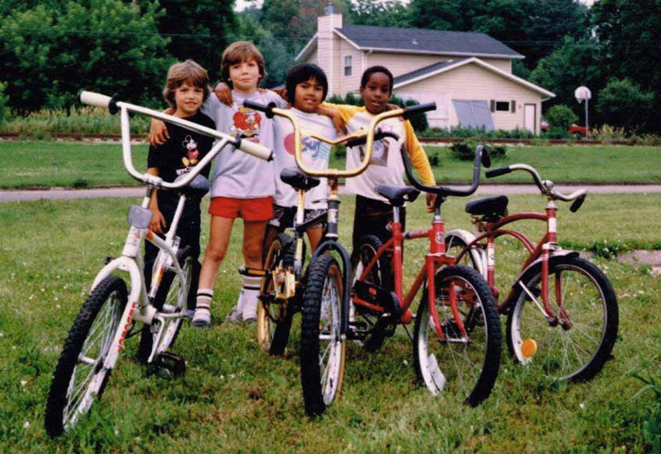 Picture of Gen X era friends with their bikes in a suburban yard.