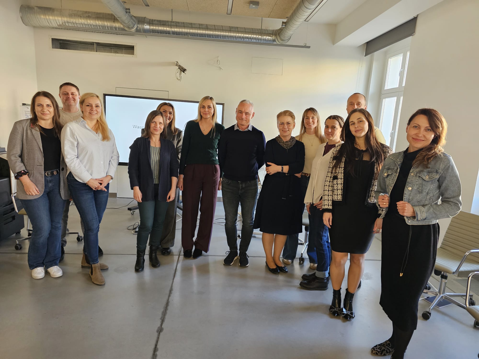 Group of participants standing together in a modern classroom after a training session, with a presentation screen visible in the background.