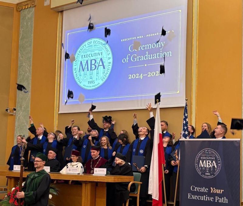 Absolwenci programu Executive MBA Uniwersytetu Ekonomicznego w Poznaniu podczas uroczystości absolutoryjnej radośnie podrzucają birety. W tle widoczny jest ekran z napisem „Ceremony of Graduation 2024–2025” oraz logo programu Executive MBA Poznań – Atlanta. 